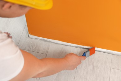 Worker using brush to paint wall with orange dye indoors, closeup