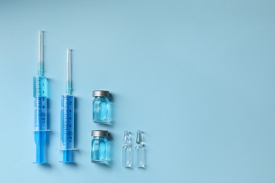 Photo of Disposable syringes with needles, ampules and vials on light blue background, flat lay. Space for text