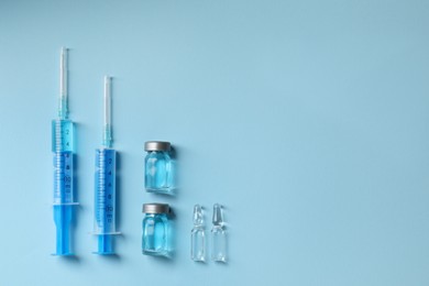 Disposable syringes with needles, ampules and vials on light blue background, flat lay. Space for text