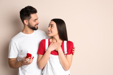 Man with engagement ring making marriage proposal to girlfriend on beige background