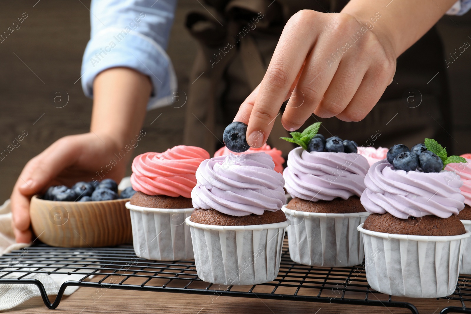 Photo of Woman decorating cupcake with fresh blueberry at wooden table, closeup