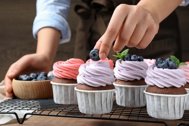 Photo of Woman decorating cupcake with fresh blueberry at wooden table, closeup