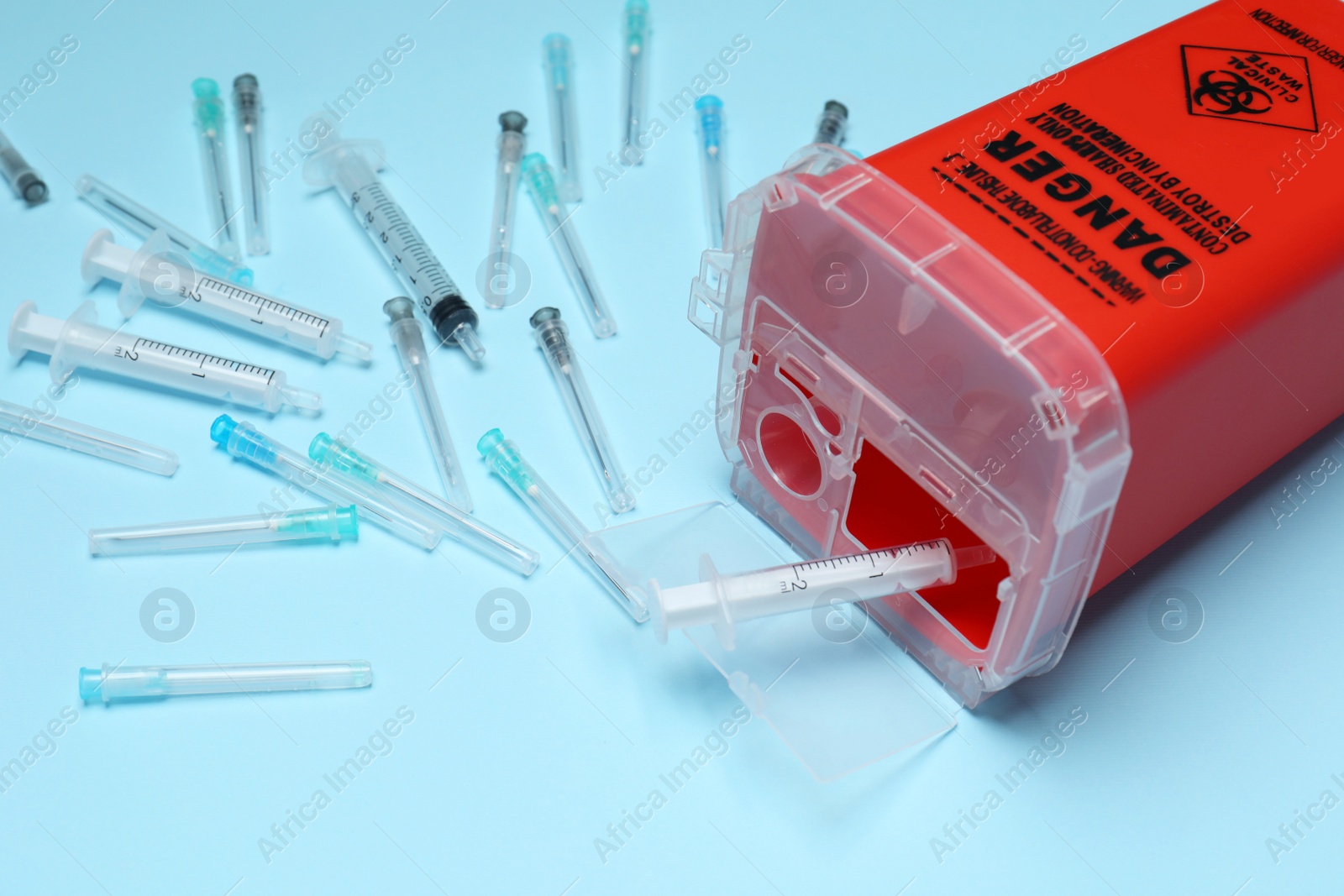 Photo of Disposable syringes, needles and sharps container on light blue background