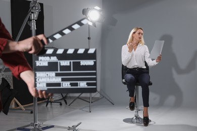 Photo of Casting call. Emotional woman performing while second assistance camera holding clapperboard against grey background in studio