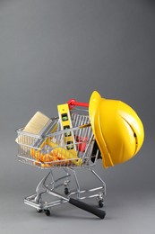 Photo of Small shopping cart with construction level, brush, gloves and hard hat on grey background