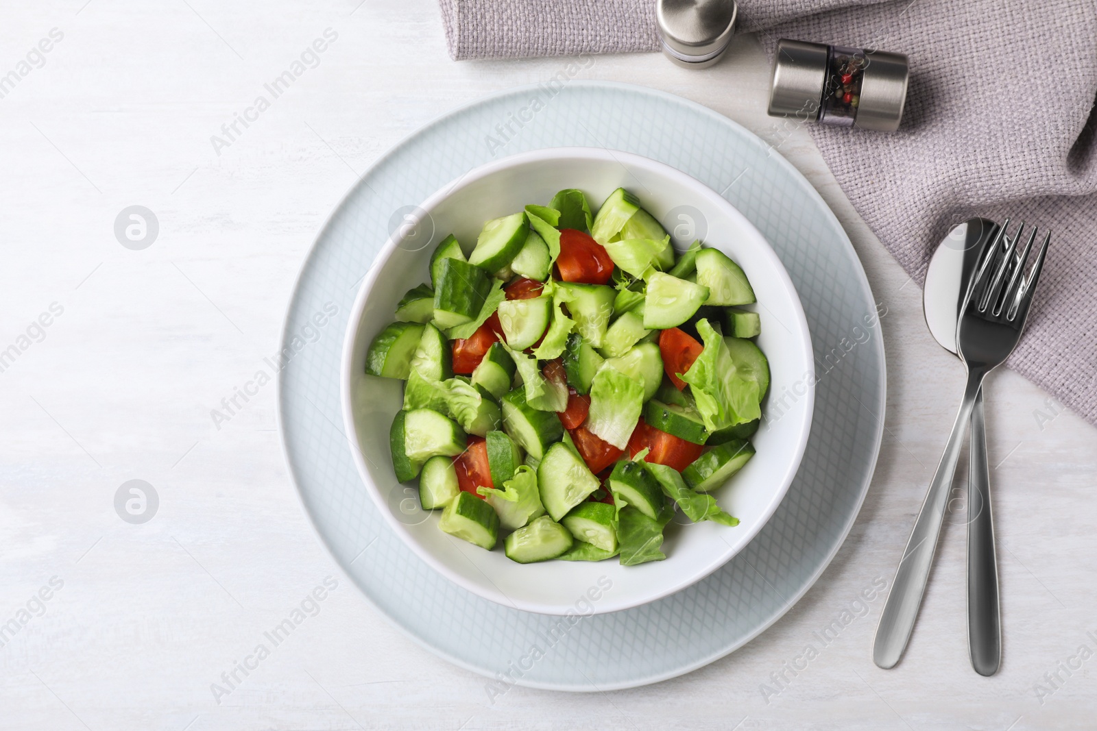 Photo of Bowl of vegetarian salad with cucumber, tomato and lettuce served on table, flat lay