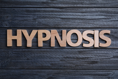 Photo of Word HYPNOTHERAPY made with wooden letters on black background, flat lay