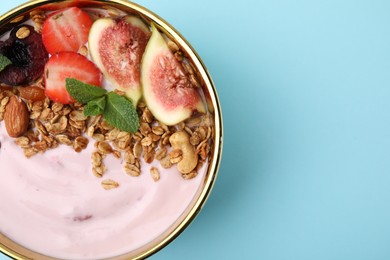 Bowl with yogurt, fruits and granola on light blue background, top view. Space for text