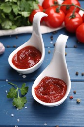 Organic ketchup in spoons, fresh tomatoes and spices on blue wooden table, closeup. Tomato sauce