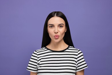 Beautiful young woman blowing kiss on purple background