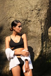 Photo of Beautiful young woman in stylish bikini near big stone outdoors