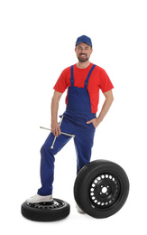 Full length portrait of professional auto mechanic with lug wrench and wheels on white background