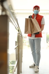 Photo of Courier in protective mask and gloves with order indoors. Restaurant delivery service during coronavirus quarantine