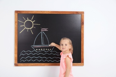 Little child drawing ship with colorful chalk on blackboard