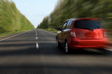 Image of Red car driving at high speed on asphalt road outdoors, motion blur effect