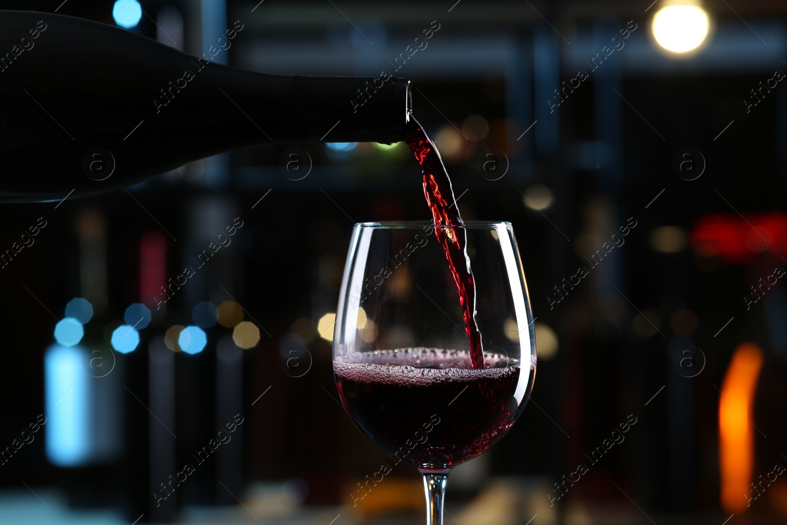 Photo of Pouring red wine from bottle into glass on blurred background, closeup