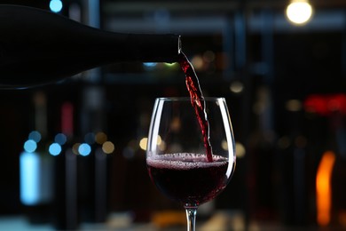 Photo of Pouring red wine from bottle into glass on blurred background, closeup