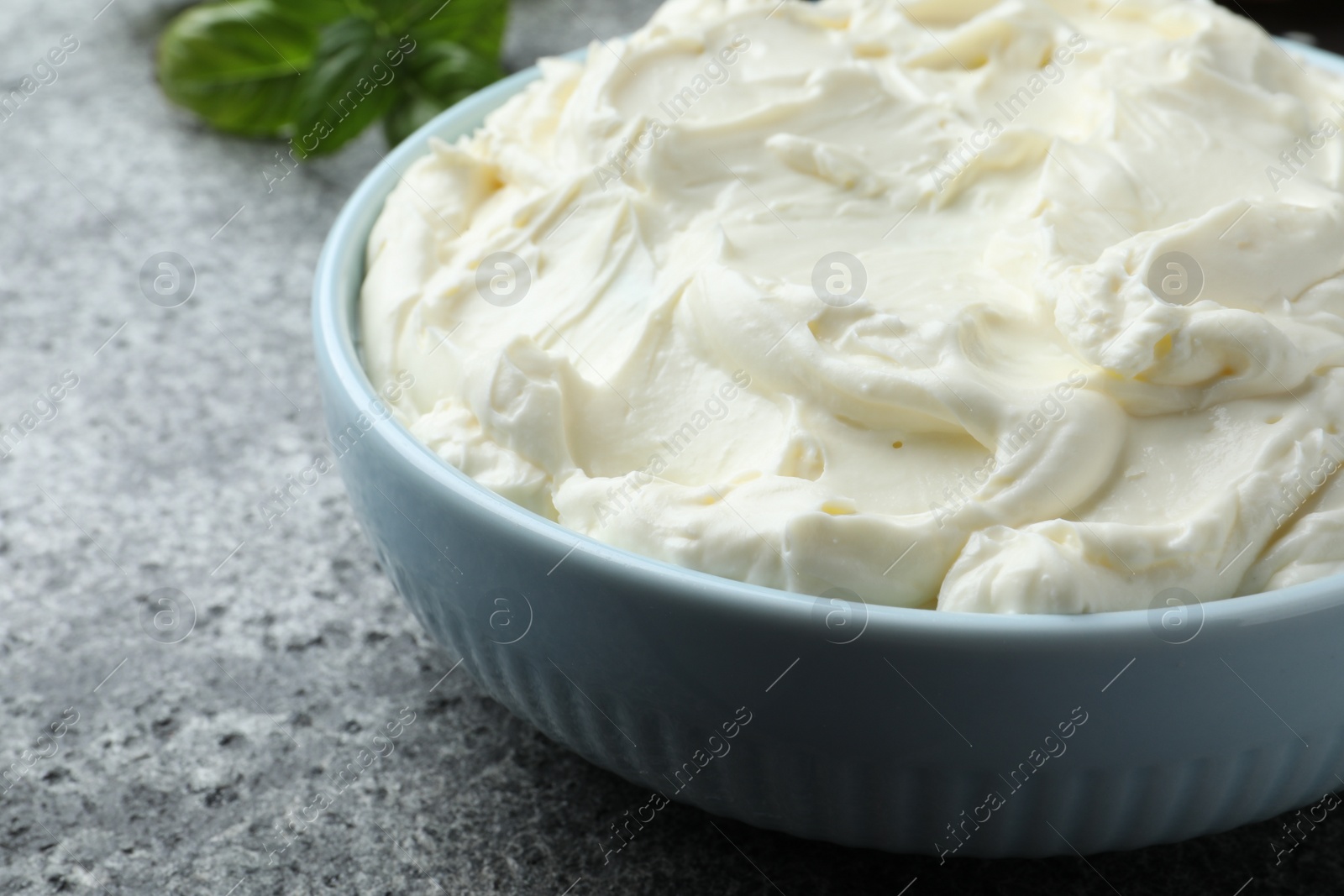 Photo of Bowl of tasty cream cheese on grey table, closeup