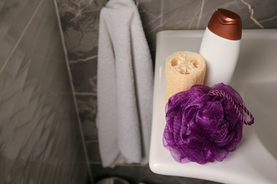 Photo of Purple shower puff, loofah sponge and bottle of body wash gel on sink in bathroom, space for text