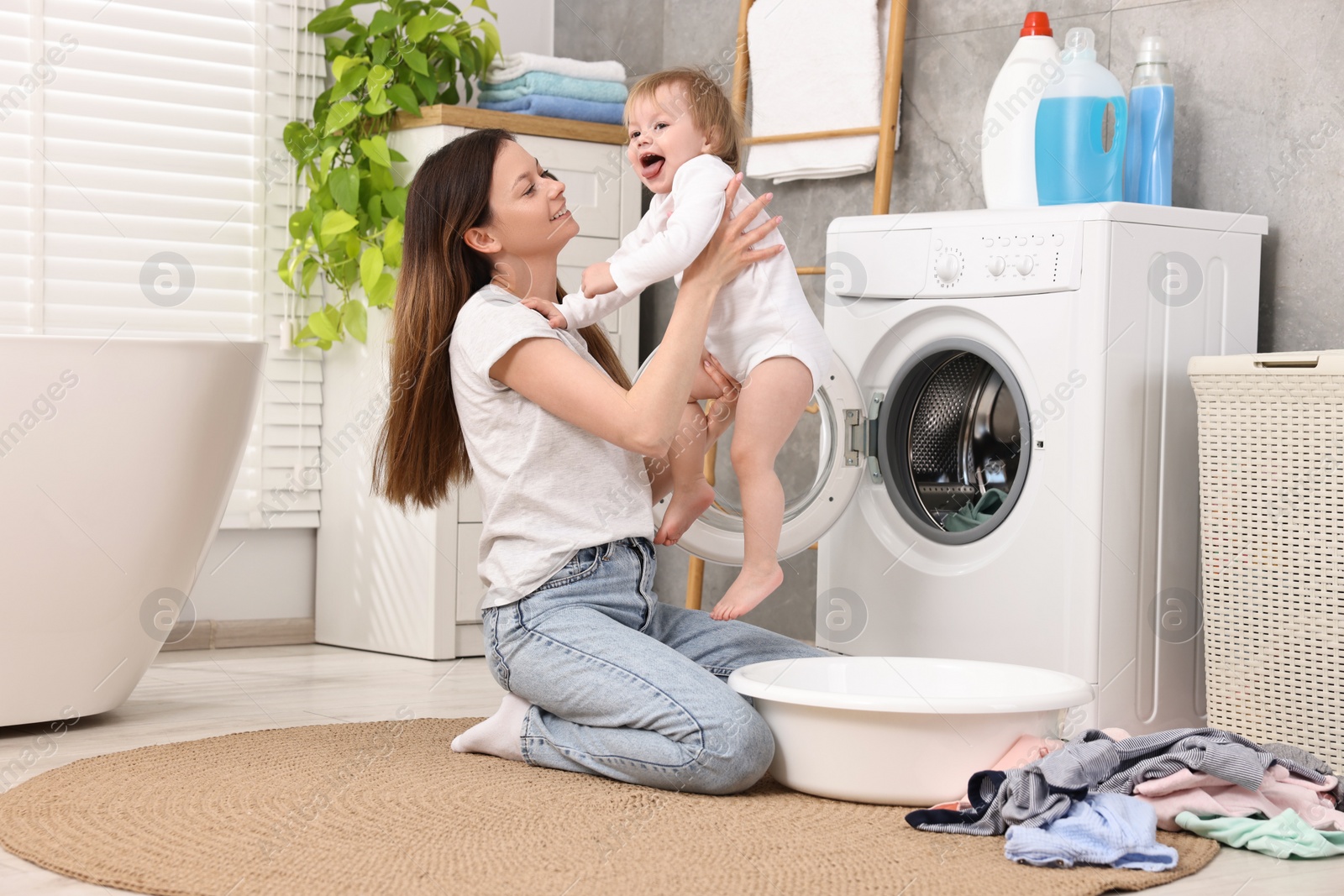 Photo of Happy mother with her daughter having fun while washing baby clothes in bathroom