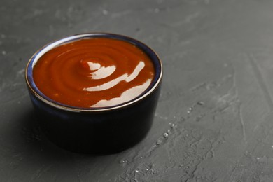 Photo of Tasty barbeque sauce in bowl on dark textured table, closeup. Space for text