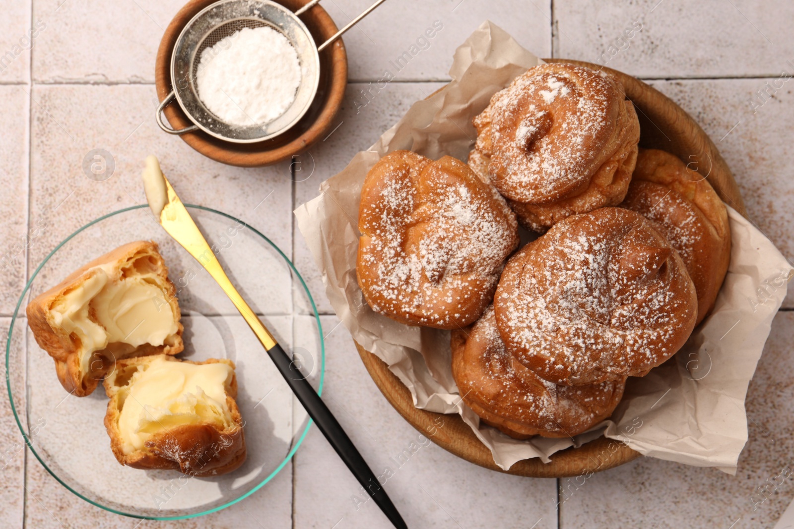 Photo of Delicious profiteroles filled with cream on white tiled table, flat lay