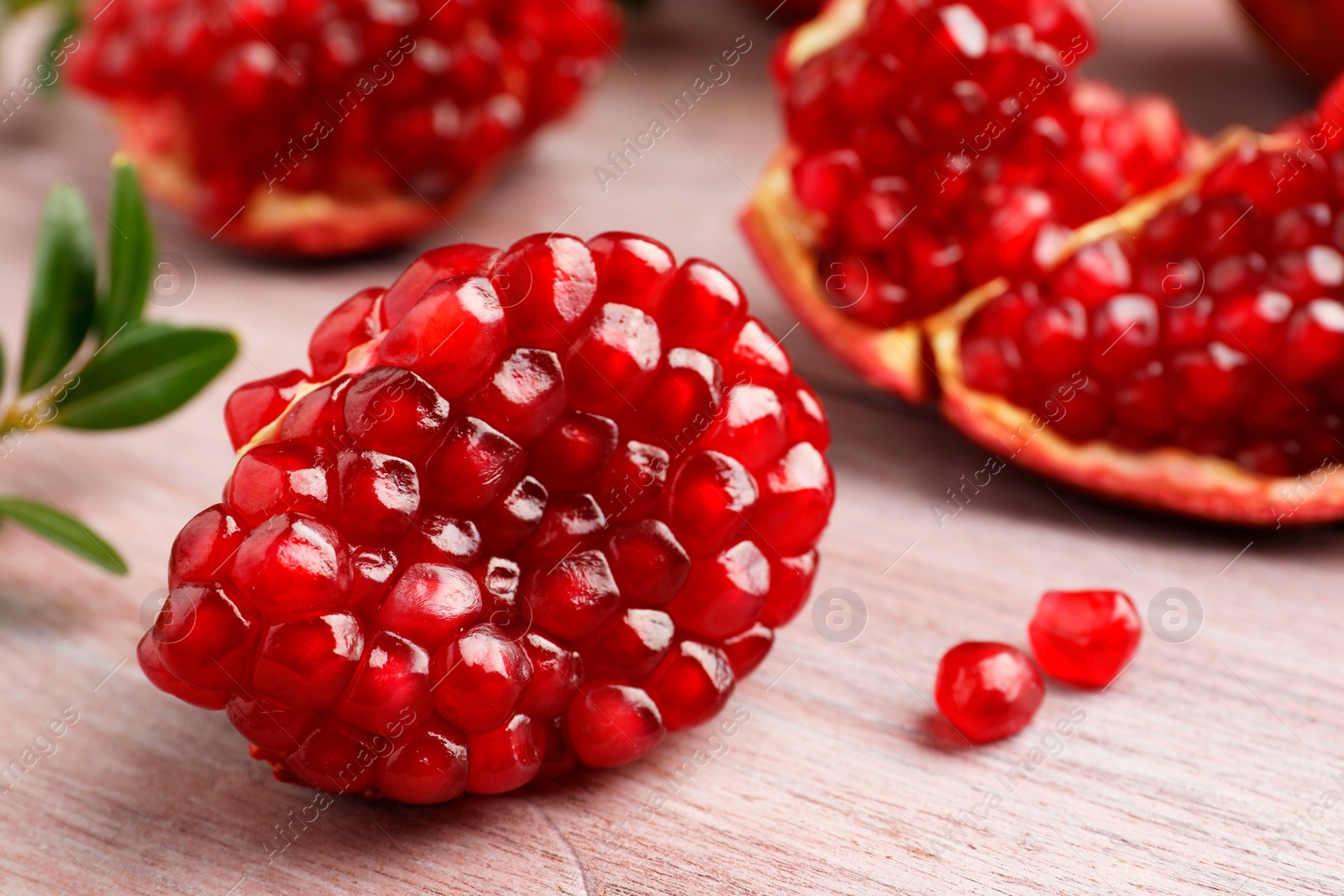 Photo of Cut fresh pomegranate and green leaves on wooden table, closeup