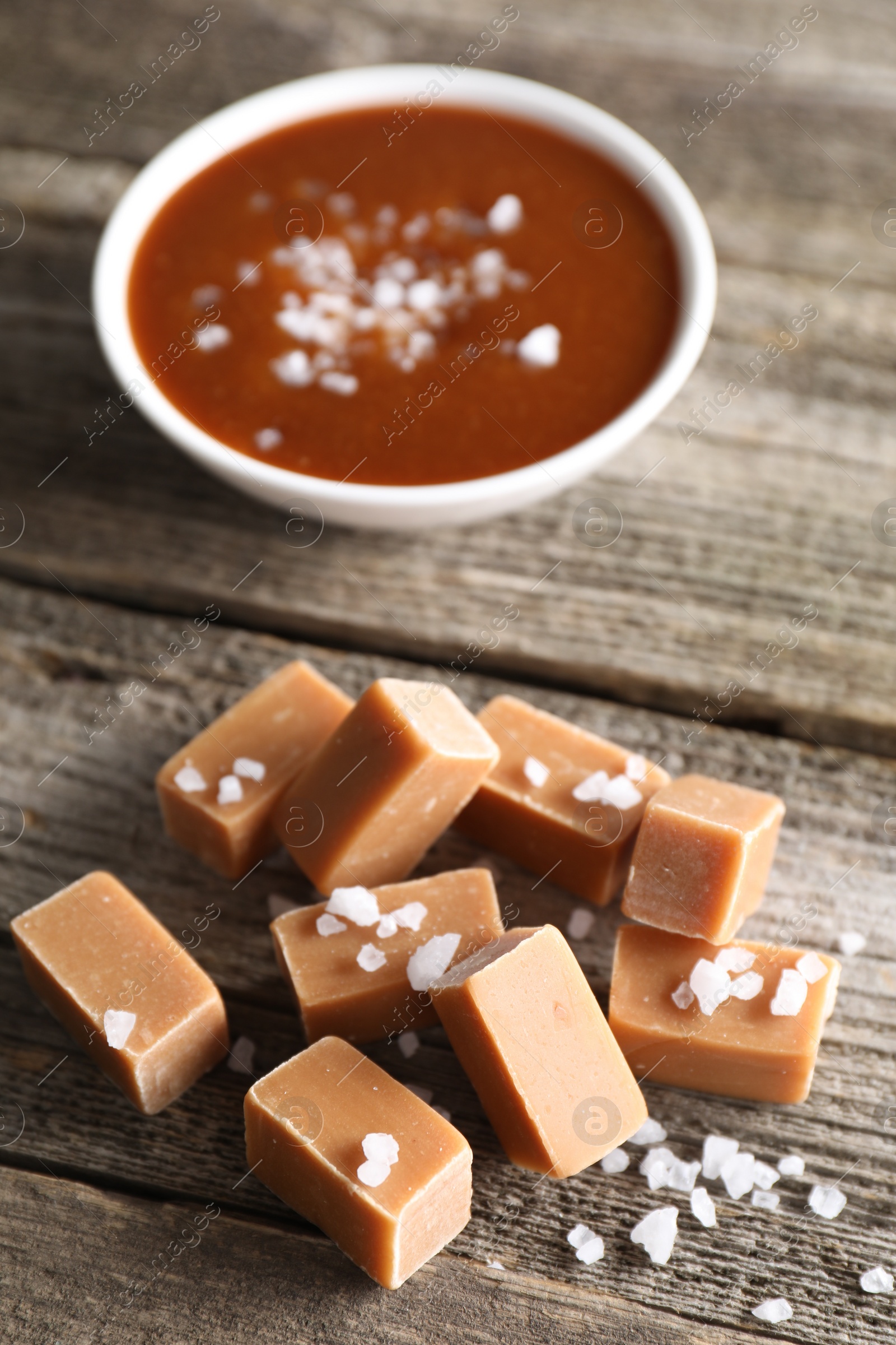 Photo of Yummy caramel candies with sea salt on wooden table, closeup