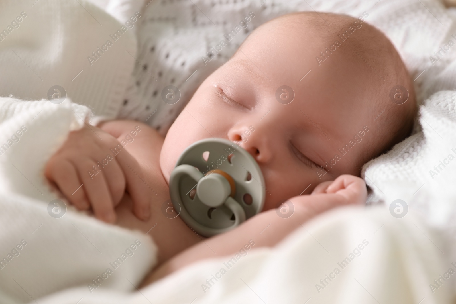 Photo of Cute newborn baby with pacifier sleeping on white blanket, closeup