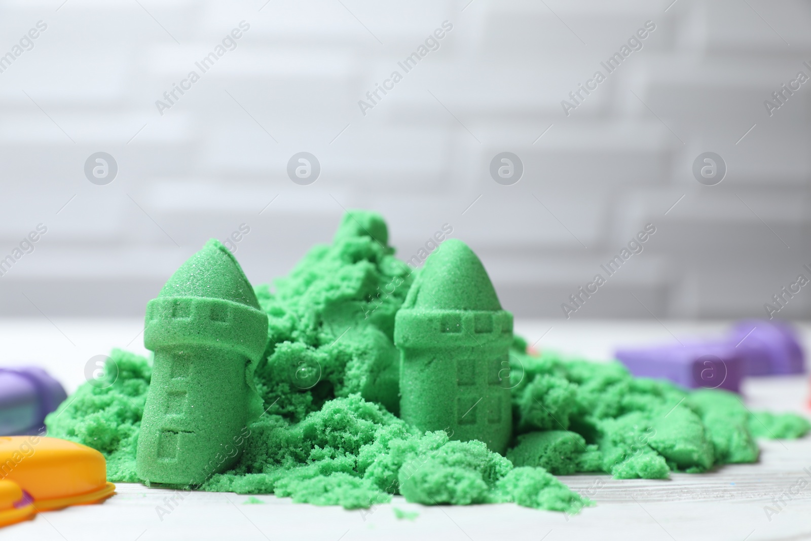 Photo of Castle figures made of green kinetic sand on white table, closeup