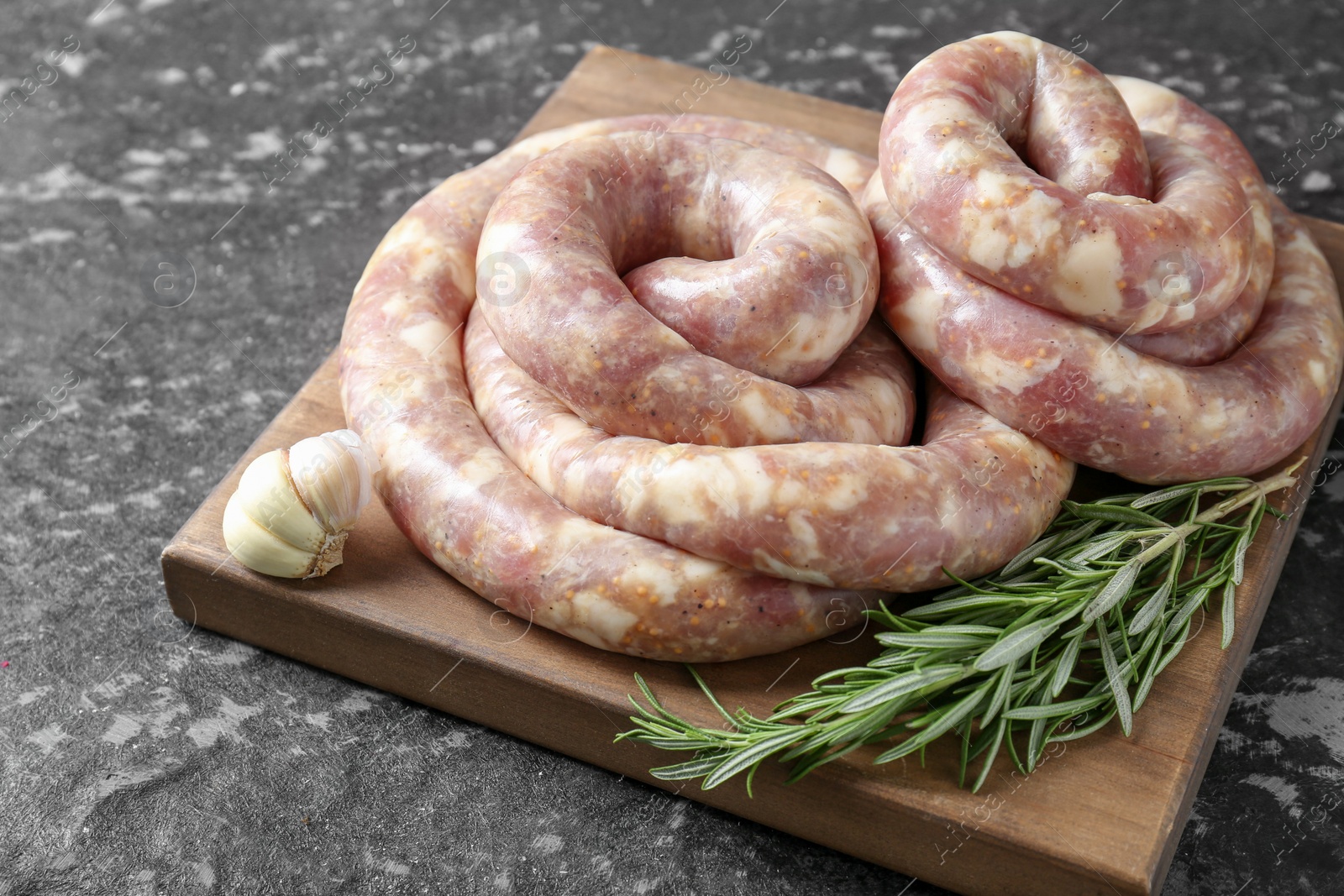 Photo of Raw homemade sausage, rosemary and garlic on grey textured table, closeup