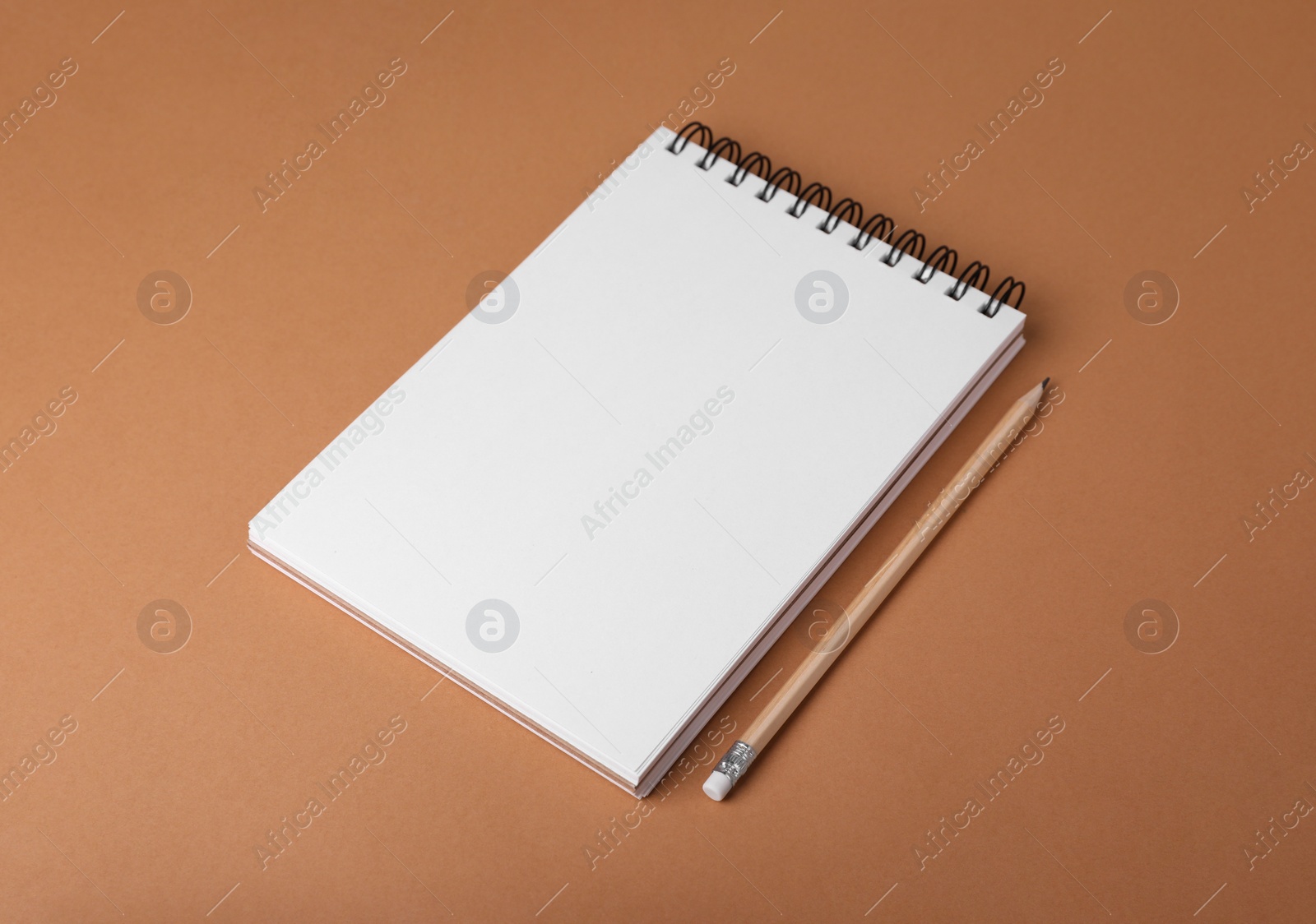 Photo of Open notebook and pencil on light brown background