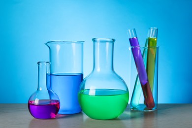 Photo of Different laboratory glassware with colorful liquids on wooden table against light blue background