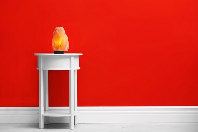 Himalayan salt lamp on table against dark red wall. Space for text