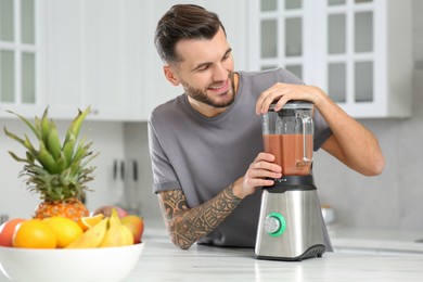 Handsome man preparing tasty smoothie at white table in kitchen