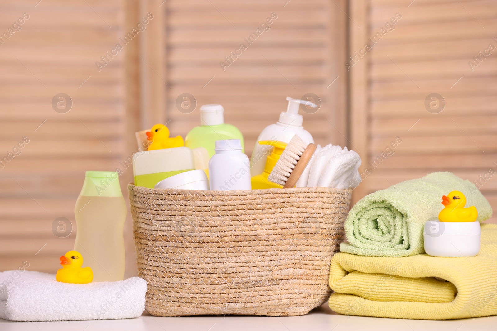 Photo of Wicker basket with baby cosmetic products, bath accessories and rubber ducks on table indoors