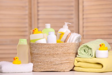 Wicker basket with baby cosmetic products, bath accessories and rubber ducks on table indoors