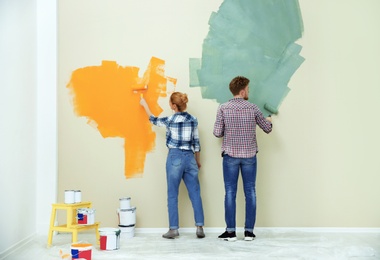 Photo of Young couple painting wall indoors. Home repair