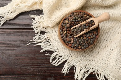 Photo of Raw lentils and scoop in bowl on wooden table, top view. Space for text