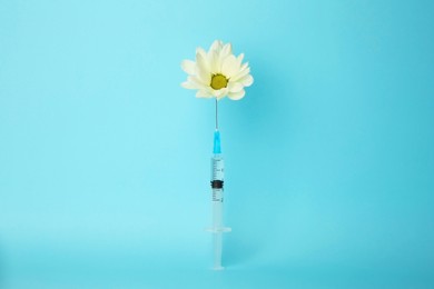 Photo of Medical syringe and beautiful chrysanthemum flower on light blue background