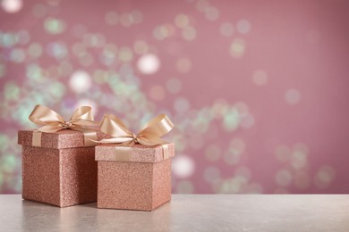 Image of Beautiful gift boxes on white table against blurred festive lights, bokeh effect. Space for text