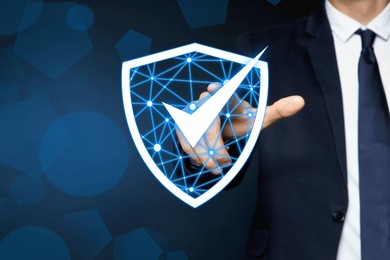 Anti-fraud security system. Man pointing at illustration of checkmark in shield on dark background, closeup. Space for text