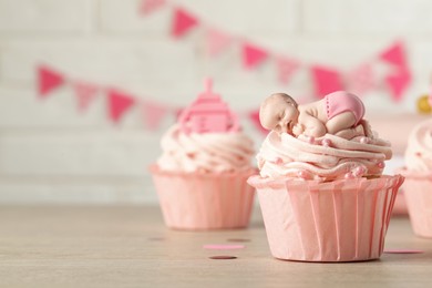 Beautifully decorated baby shower cupcakes with cream and girl toppers on wooden table. Space for text