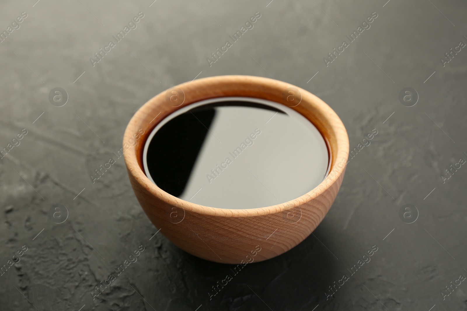 Photo of Soy sauce in wooden bowl on black textured table