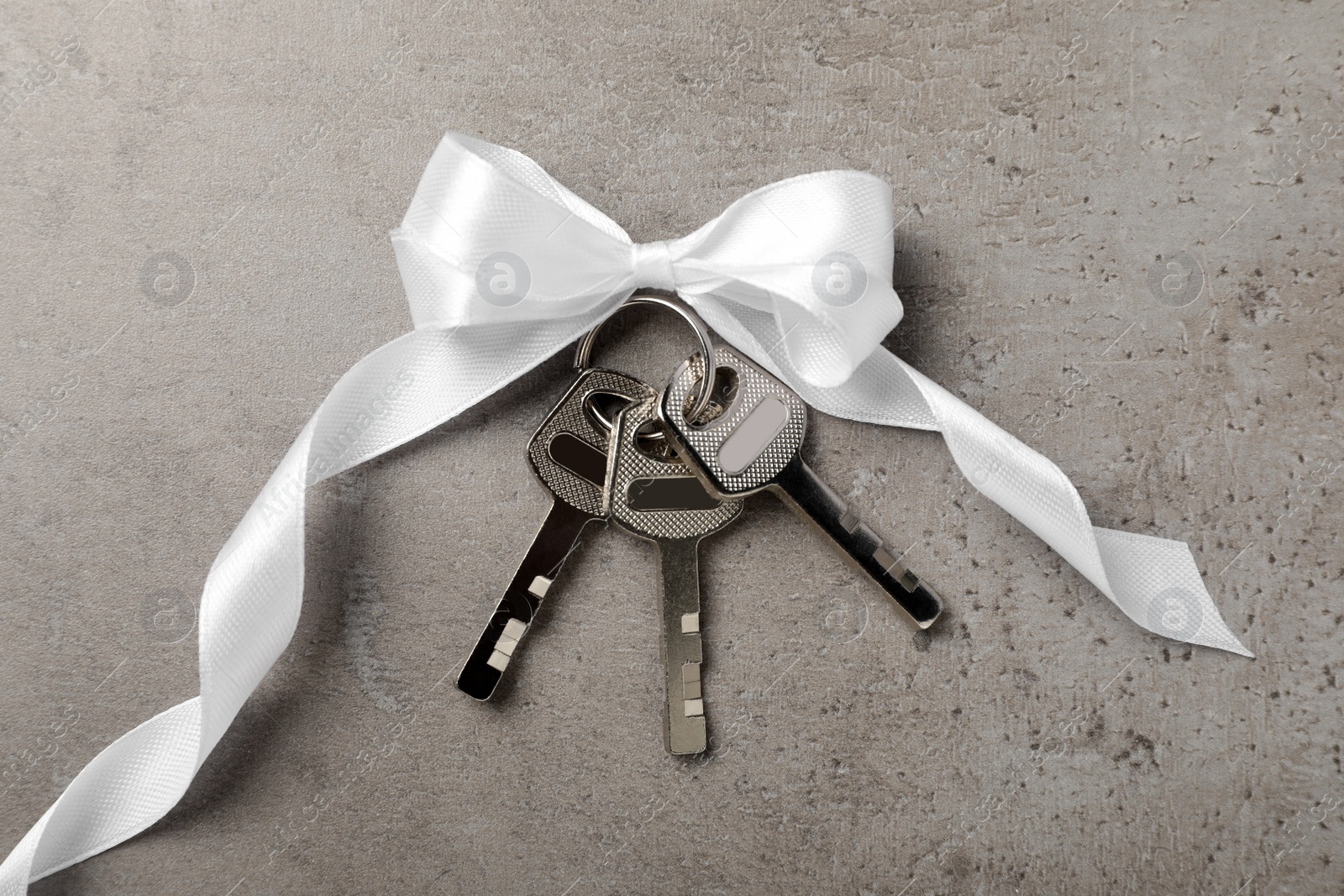 Photo of Keys with white bow on grey table, top view. Housewarming party