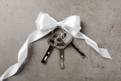 Keys with white bow on grey table, top view. Housewarming party