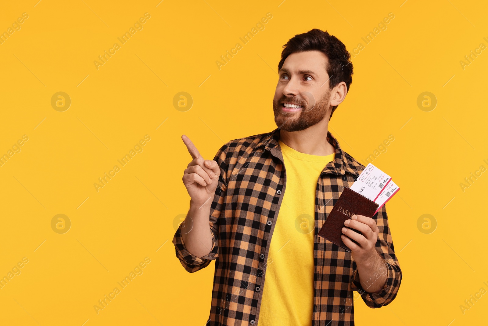 Photo of Smiling man with passport and tickets pointing at something on yellow background. Space for text