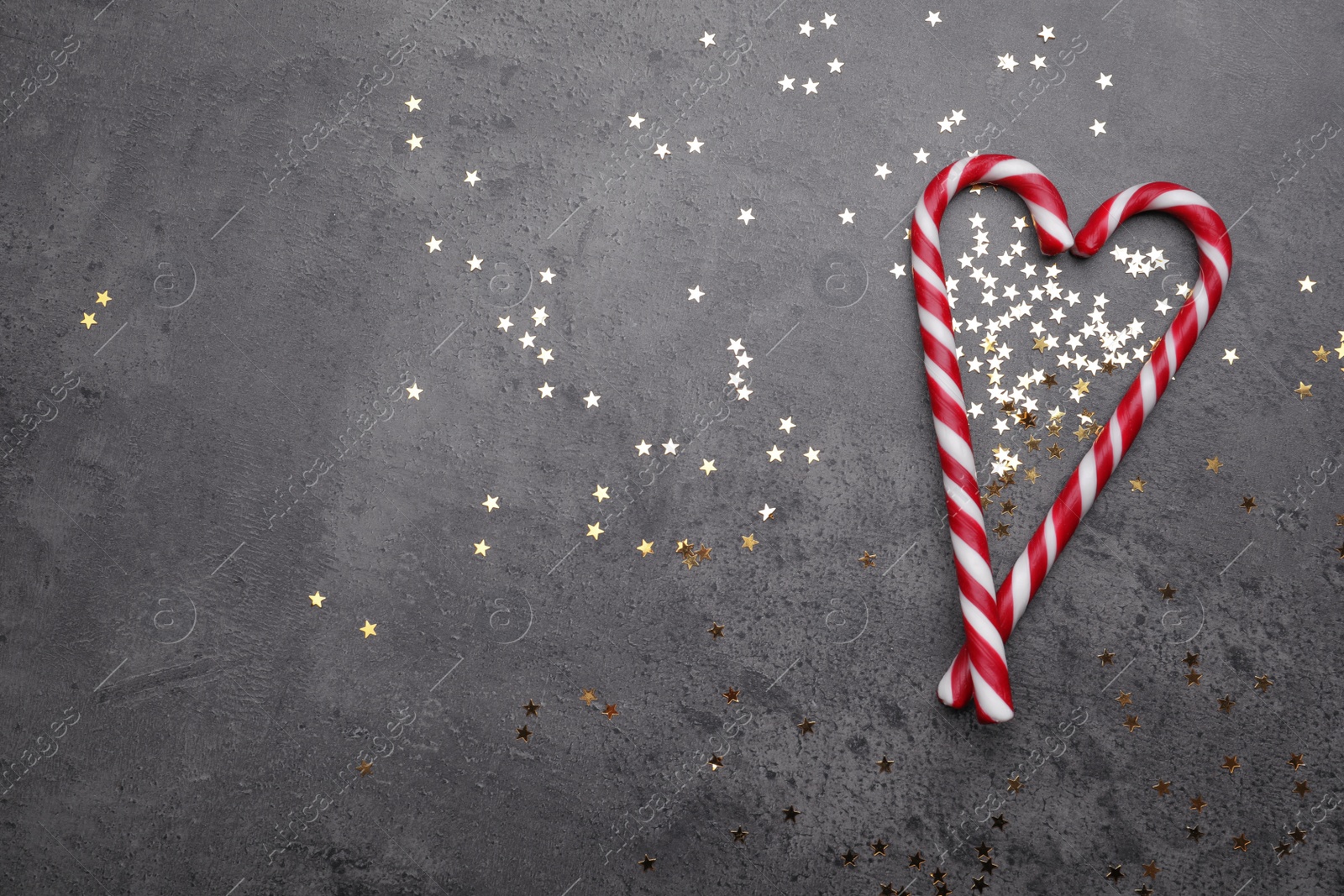 Photo of Heart made of sweet Christmas candy canes and shiny confetti on grey background, flat lay. Space for text