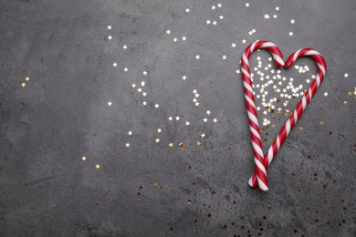 Photo of Heart made of sweet Christmas candy canes and shiny confetti on grey background, flat lay. Space for text