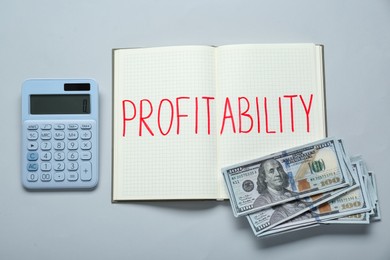 Photo of Notebook with word Profitability, calculator and banknotes on light grey background, flat lay. Profit concept